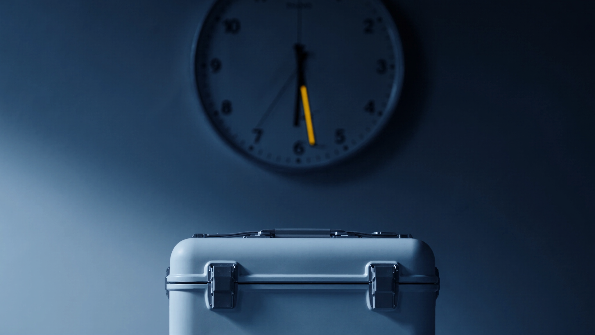 A sealed secure medical transit case at a clinical handover point beneath a wall clock